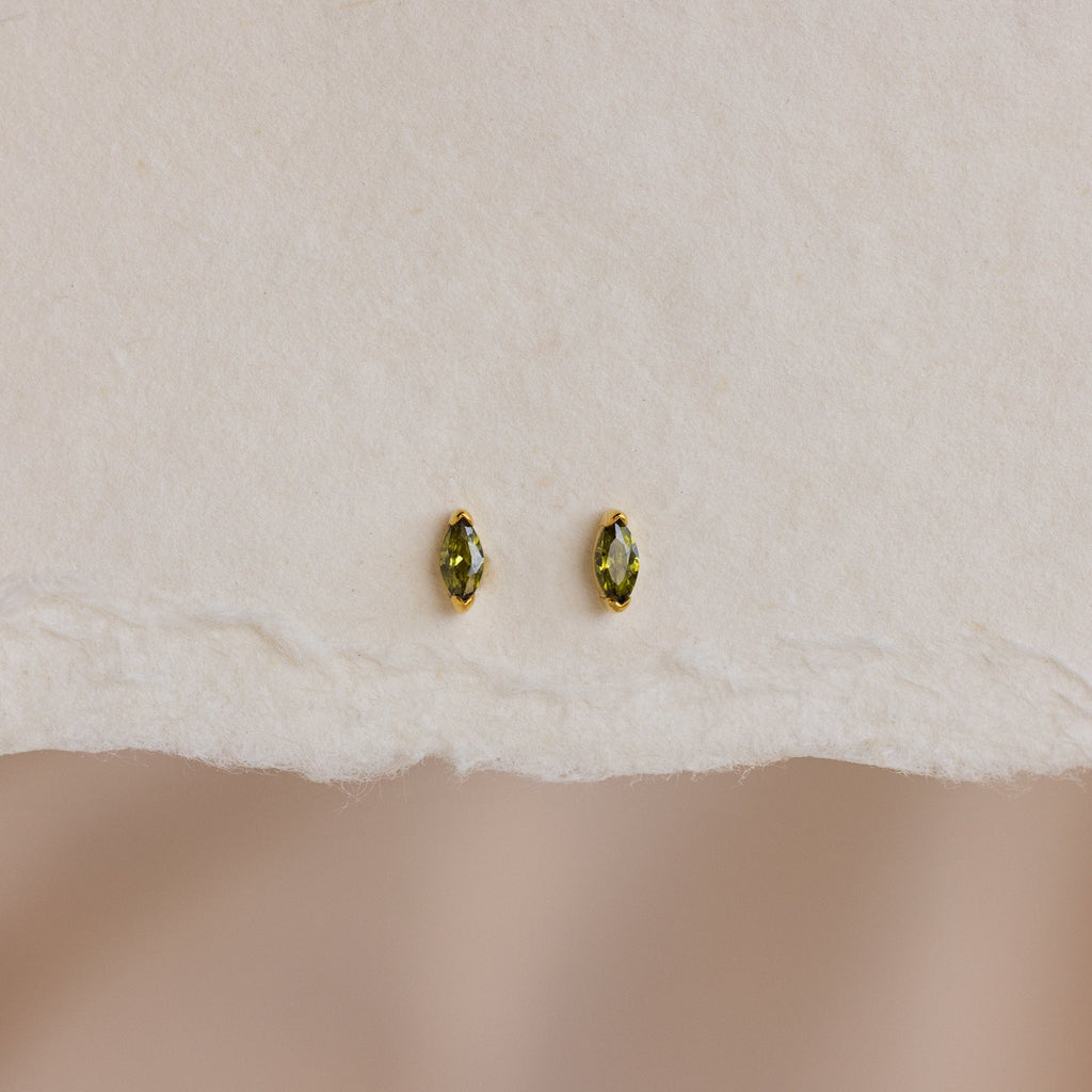 A pair of Marquise Birthstone Studs with personalized green marquise-cut gemstones, shown on textured white paper.