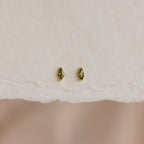 A pair of Marquise Birthstone Studs with personalized green marquise-cut gemstones, shown on textured white paper.