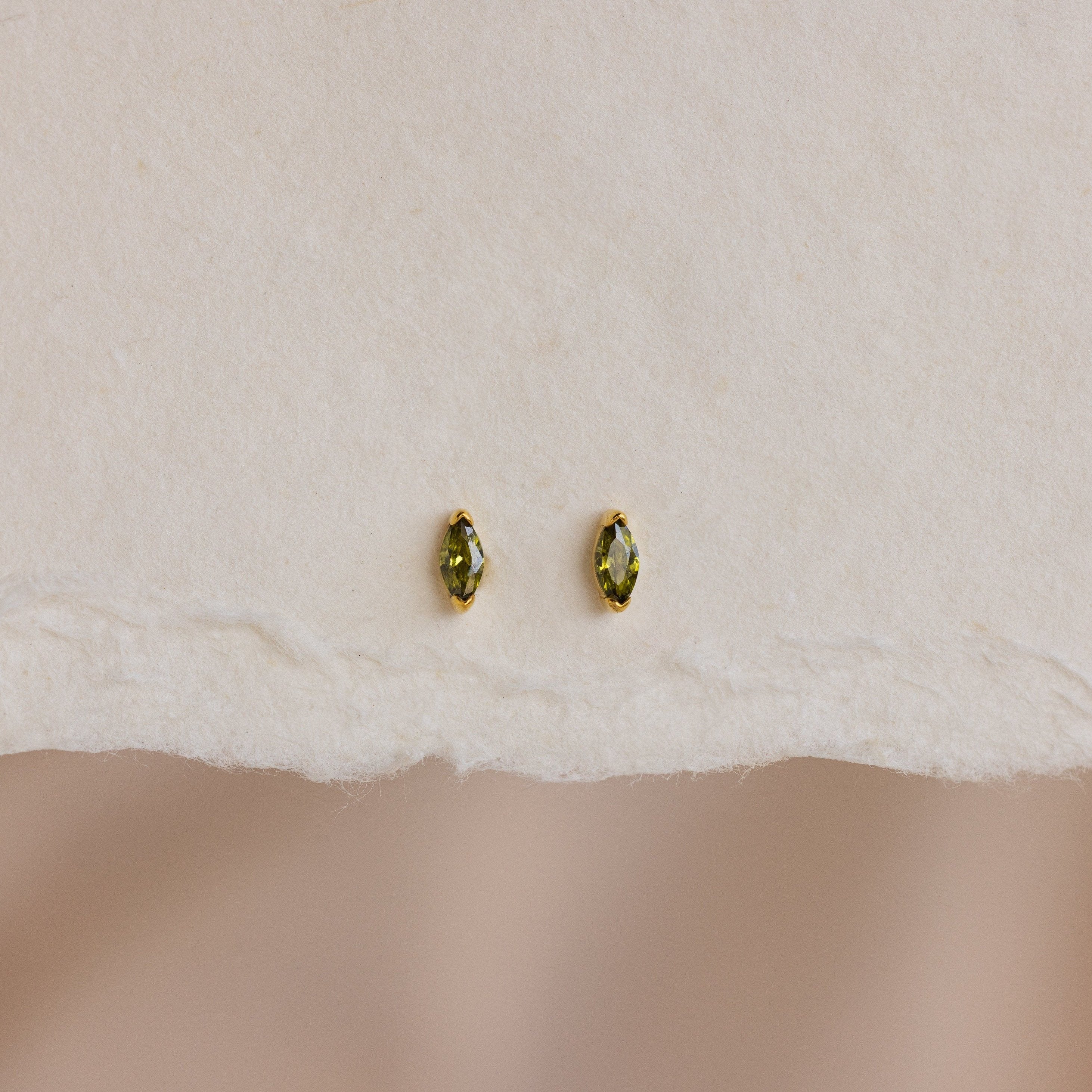A pair of Marquise Birthstone Studs with personalized green marquise-cut gemstones, shown on textured white paper.