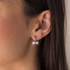 Close-up of a woman's ear wearing Diamond Bow Huggies—silver hoop earrings featuring a delicate bow-shaped design.