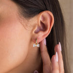 A close-up of a woman's ear showcases the Diamond Bow Huggies, gold hoop earrings featuring an elegant bow-shaped diamond accent.