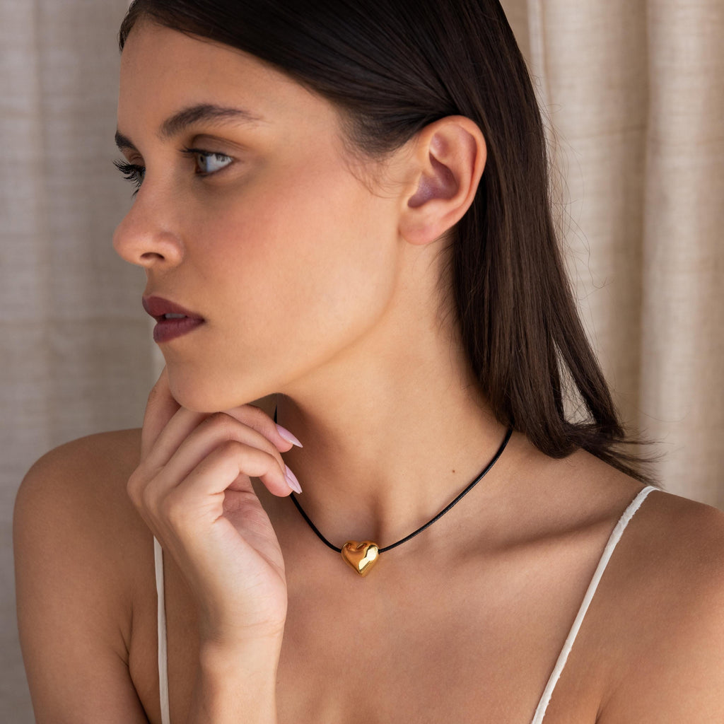 Woman with straight dark hair wearing a Chunky Puff Heart Necklace and a white top, looking to the side.