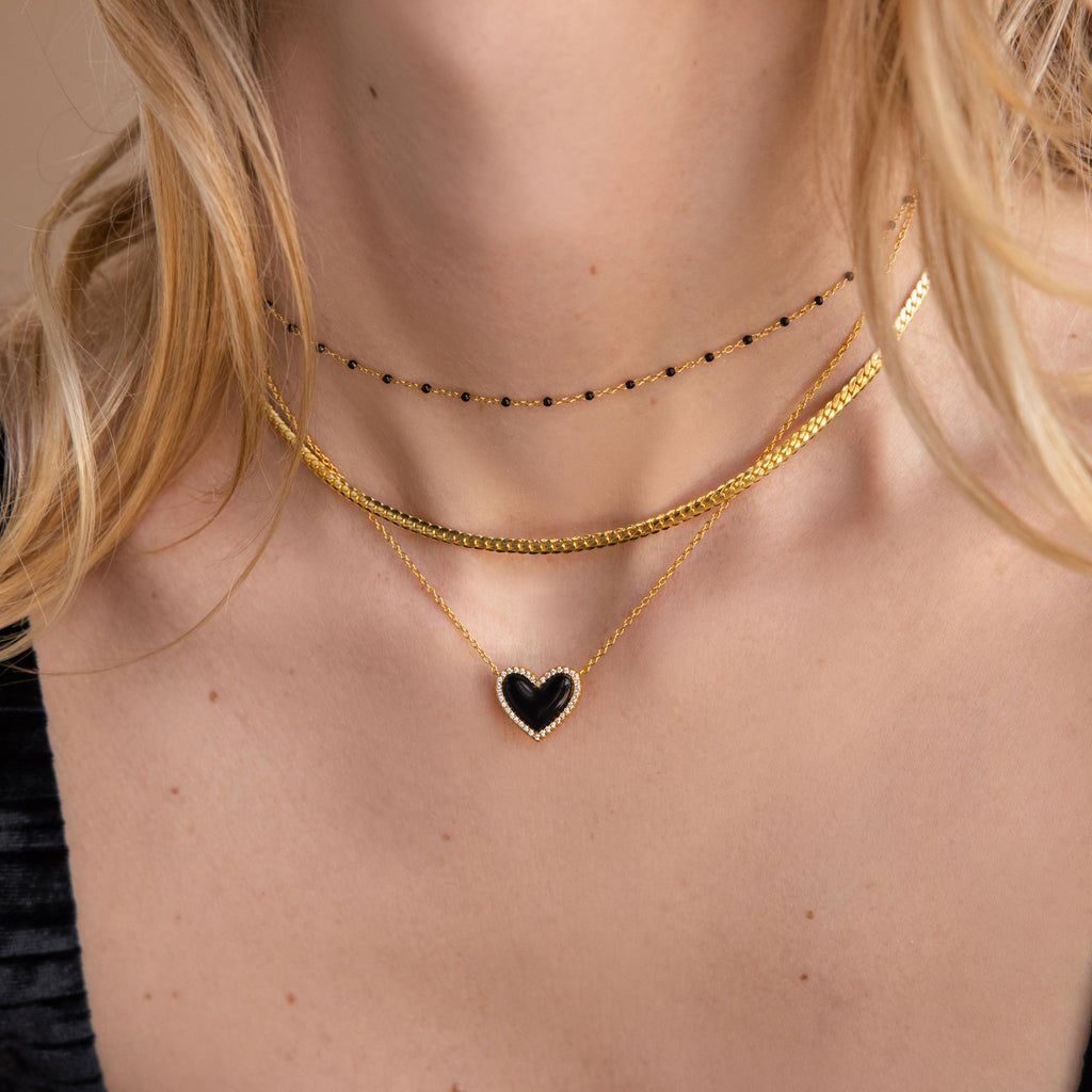 Woman wearing layered gold necklaces, including a coquette necklace and the Pavé Onyx Puff Heart Necklace in Sterling Silver, paired with a chic black choker.
