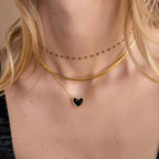 Woman wearing layered gold necklaces, including a coquette necklace and the Pavé Onyx Puff Heart Necklace in Sterling Silver, paired with a chic black choker.