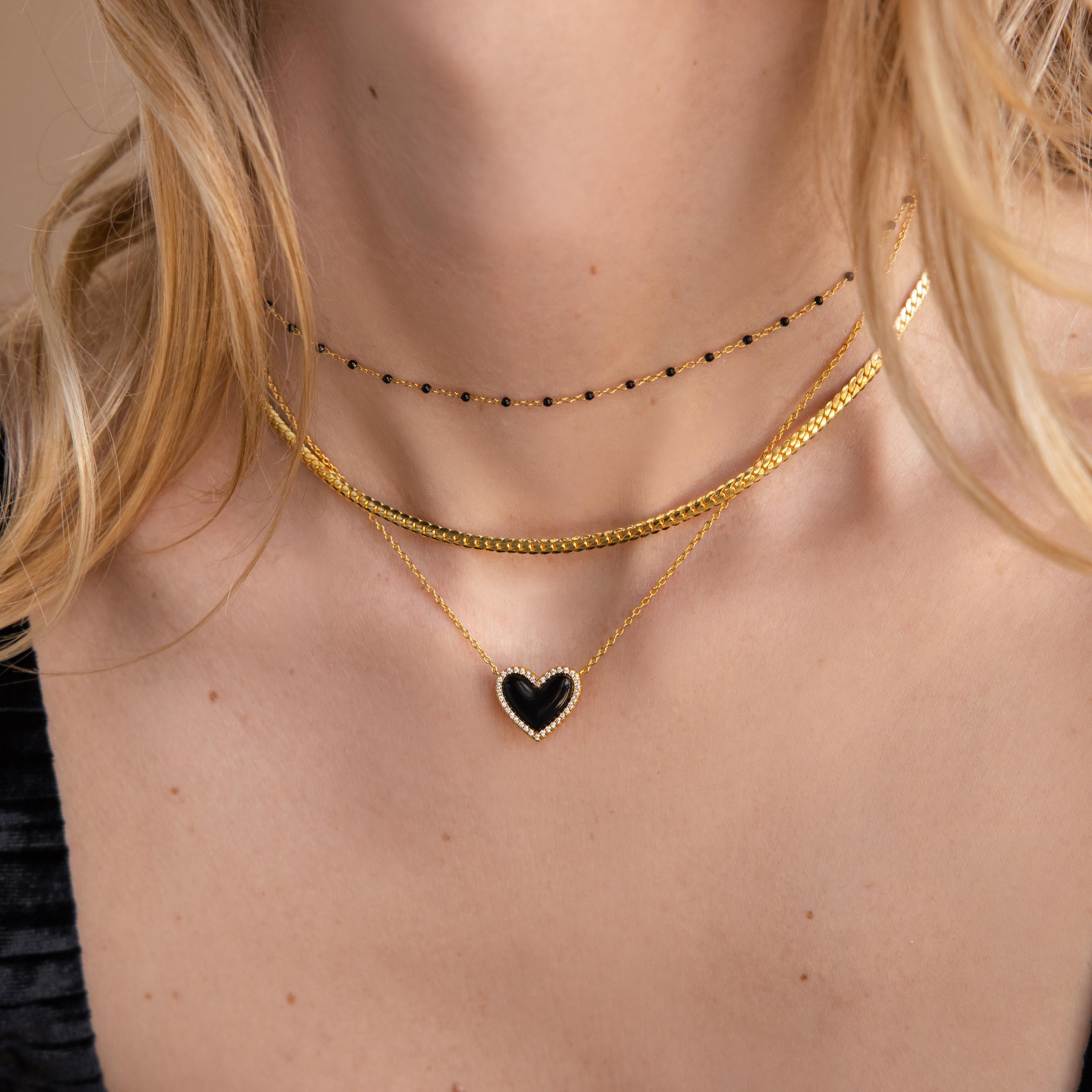 Woman wearing layered gold necklaces, including a coquette necklace and the Pavé Onyx Puff Heart Necklace in Sterling Silver, paired with a chic black choker.