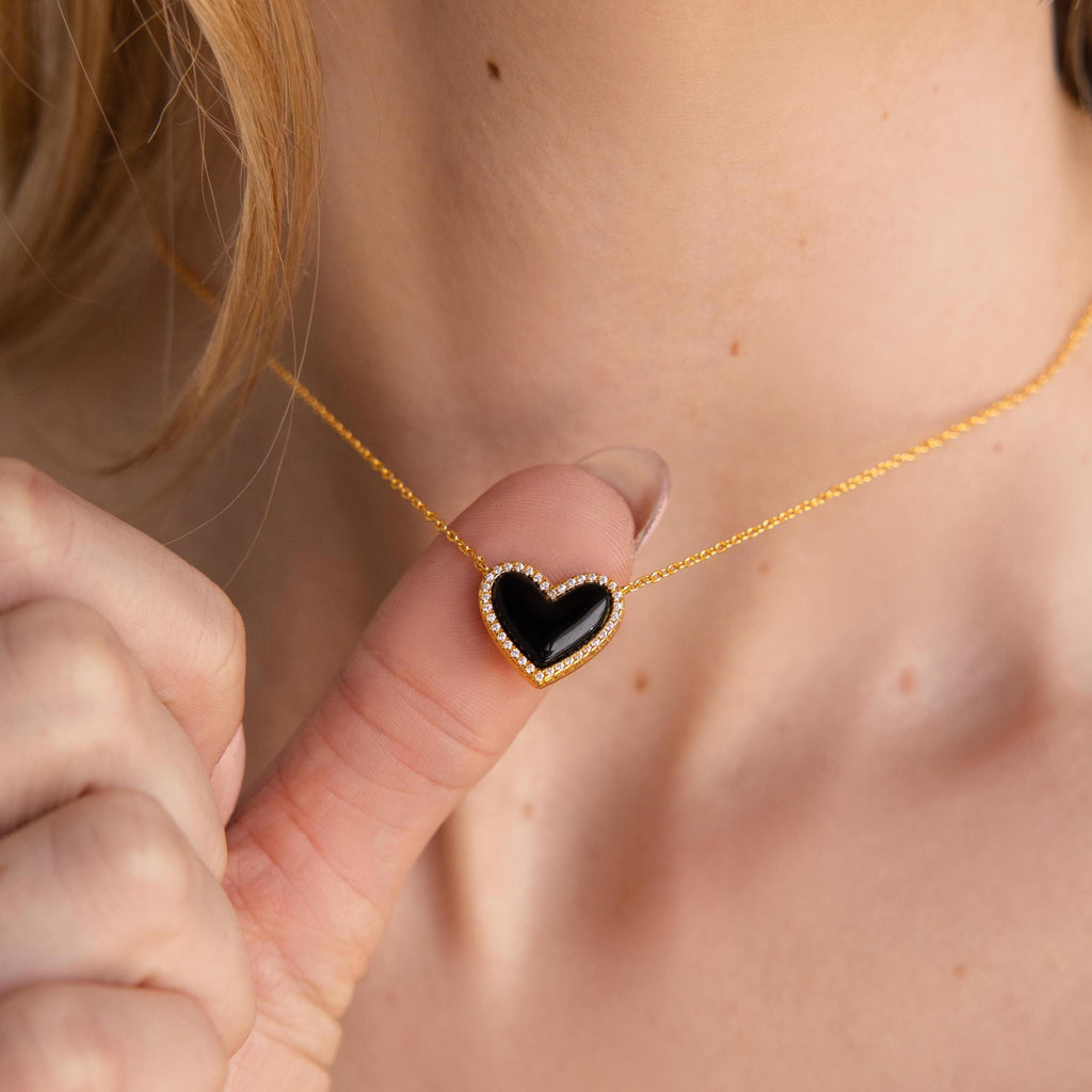 A person showcases the Pave Onyx Puff Heart Necklace, featuring a black heart pendant near their neck for an effortlessly coquette look.