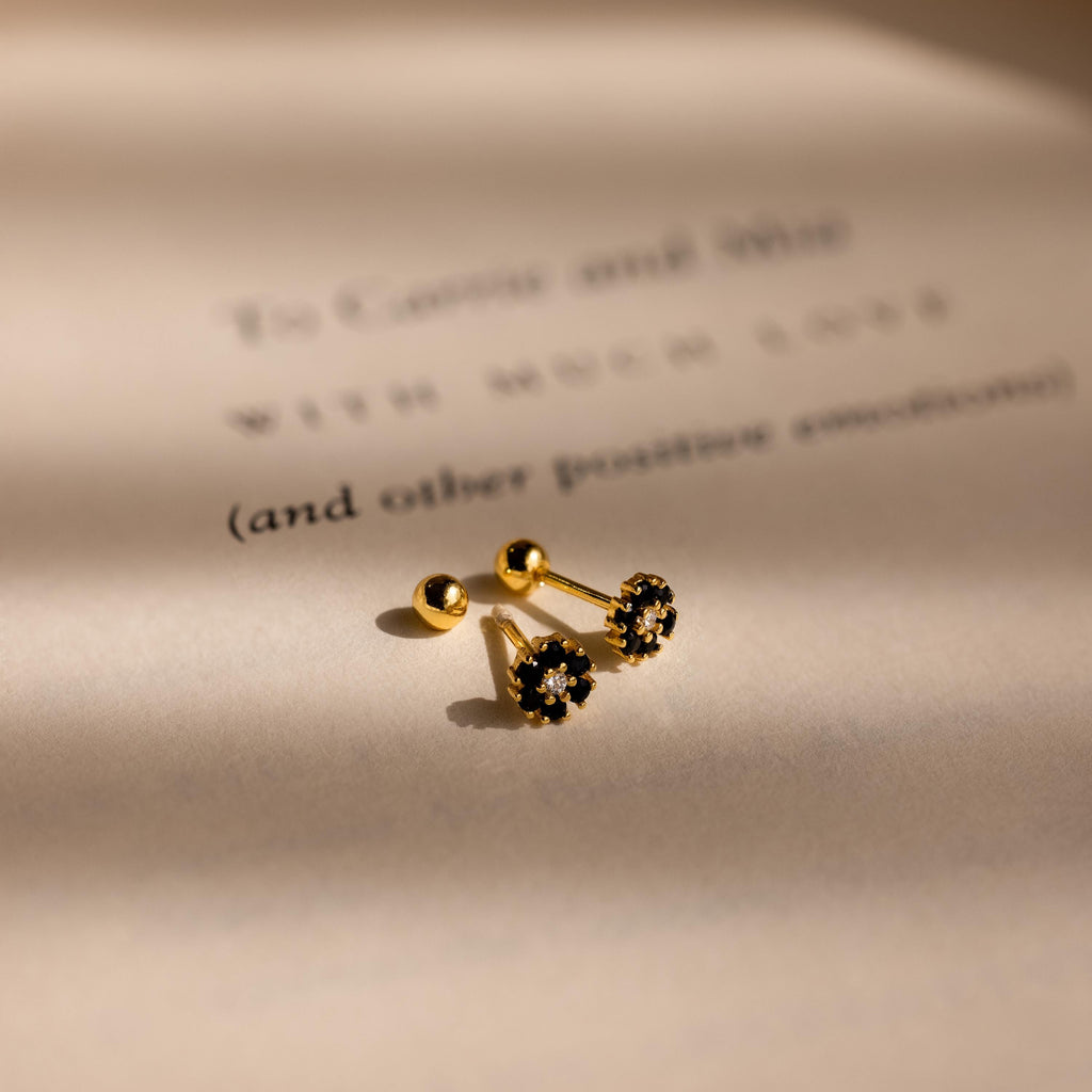 The Onyx Flower Studs sit on a softly lit, blurred text background, showcasing their elegant black onyx accents.