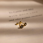 The Onyx Flower Studs sit on a softly lit, blurred text background, showcasing their elegant black onyx accents.