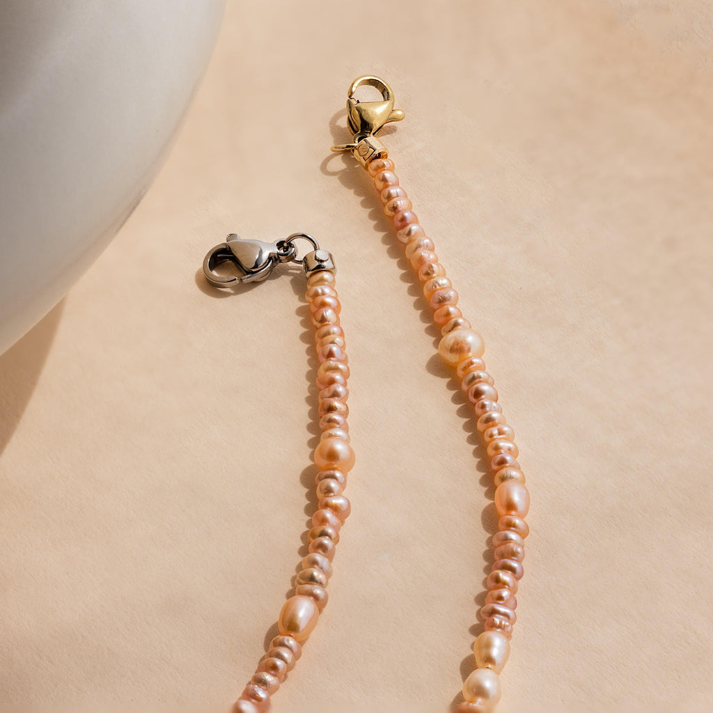 The Blush Pearl Beaded Necklace features two strands with gold and silver clasps, shown on a soft beige background, bringing timeless elegance to your collection.