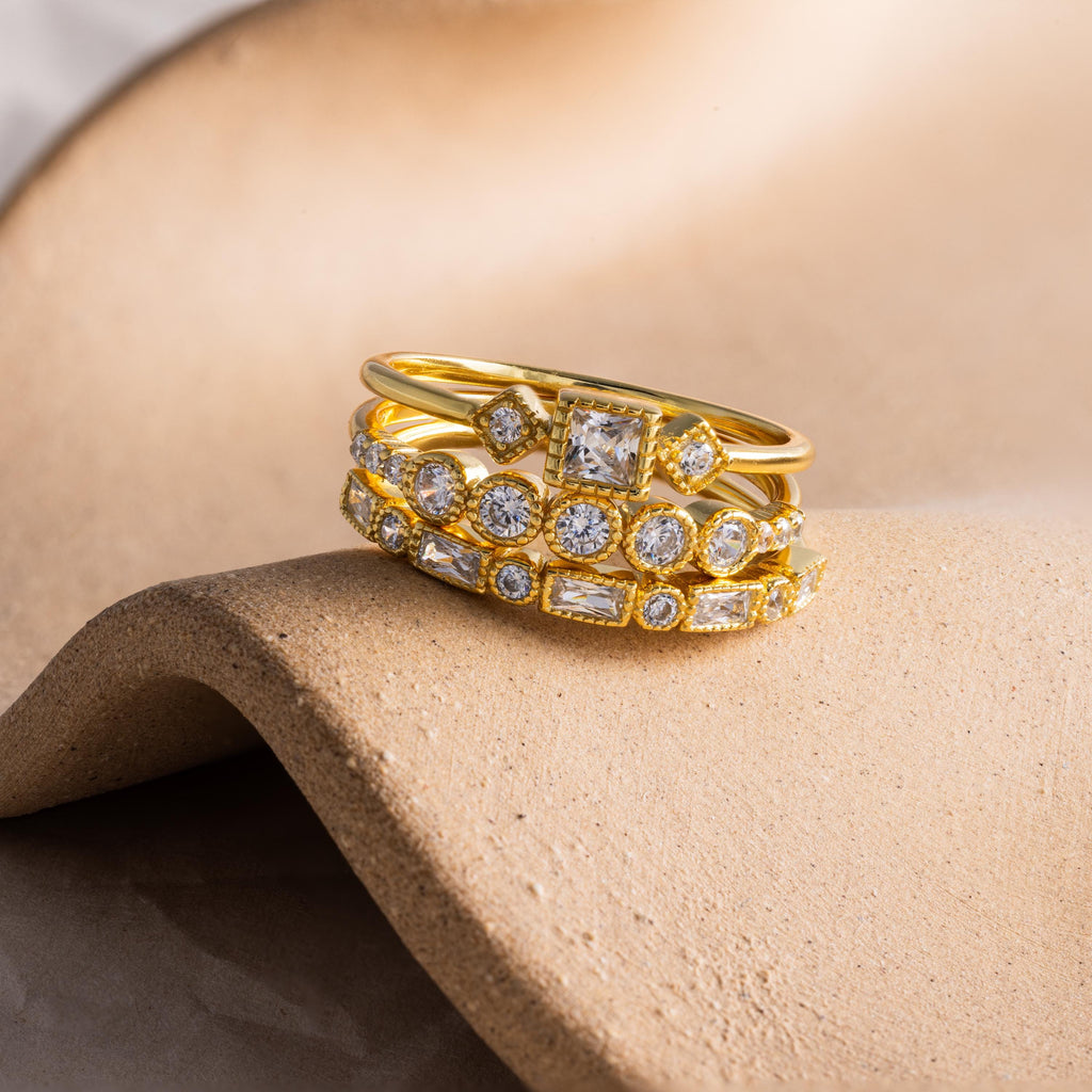 Gold Art Deco diamond ring set featuring various cut stones in stacked bands, displayed on a sculpted beige surface.