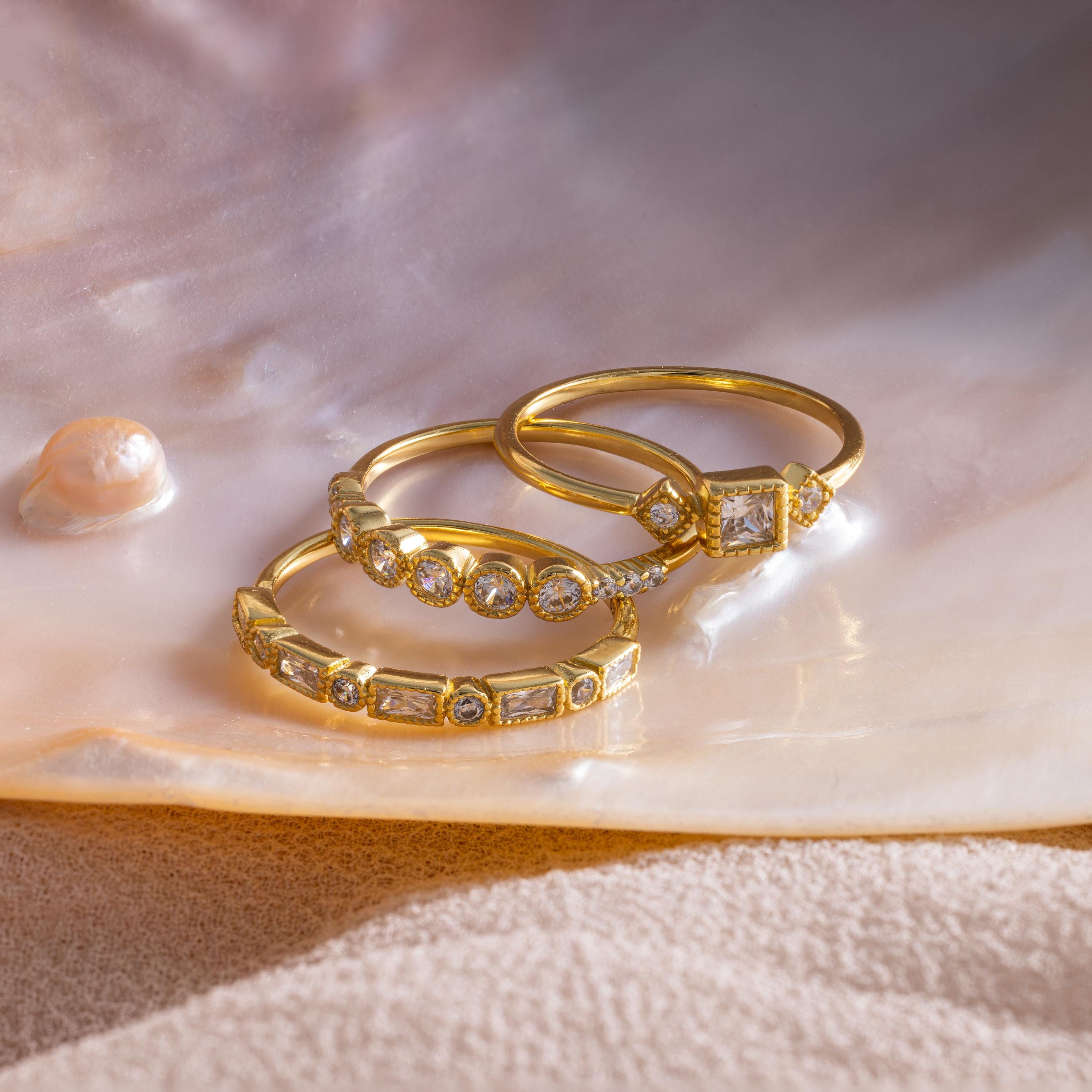 The Art Deco Diamond Ring Set, featuring three gold rings with diamonds, is displayed on a pearly seashell background to evoke timeless vintage glamour.