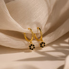 Onyx Flower Huggies: gold hoop earrings with small black and white floral charms, displayed on soft, sheer white fabric.