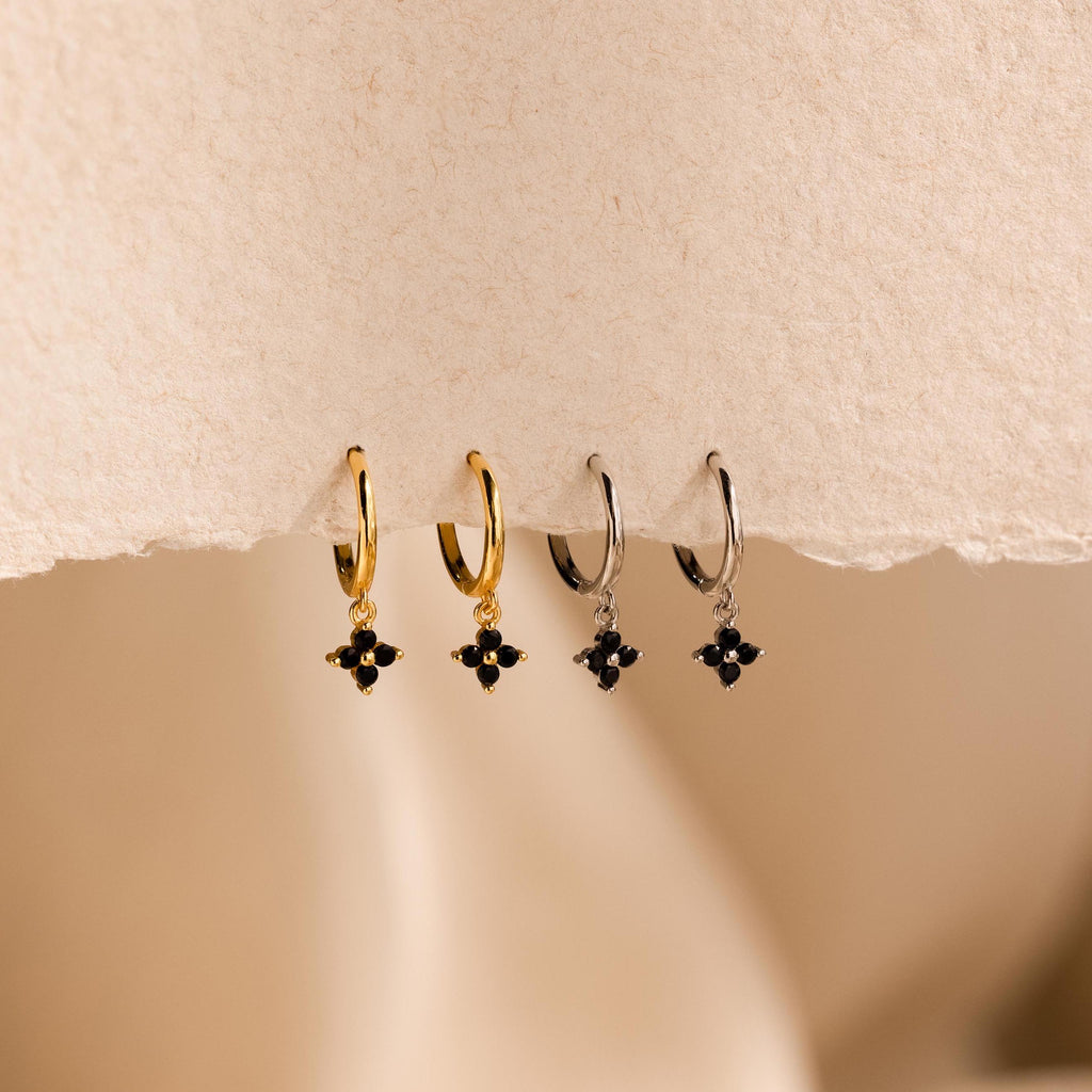 Two pairs of Black Ivy Flower Huggies—small hoop earrings in gold and silver, each adorned with a black gemstone cluster charm.