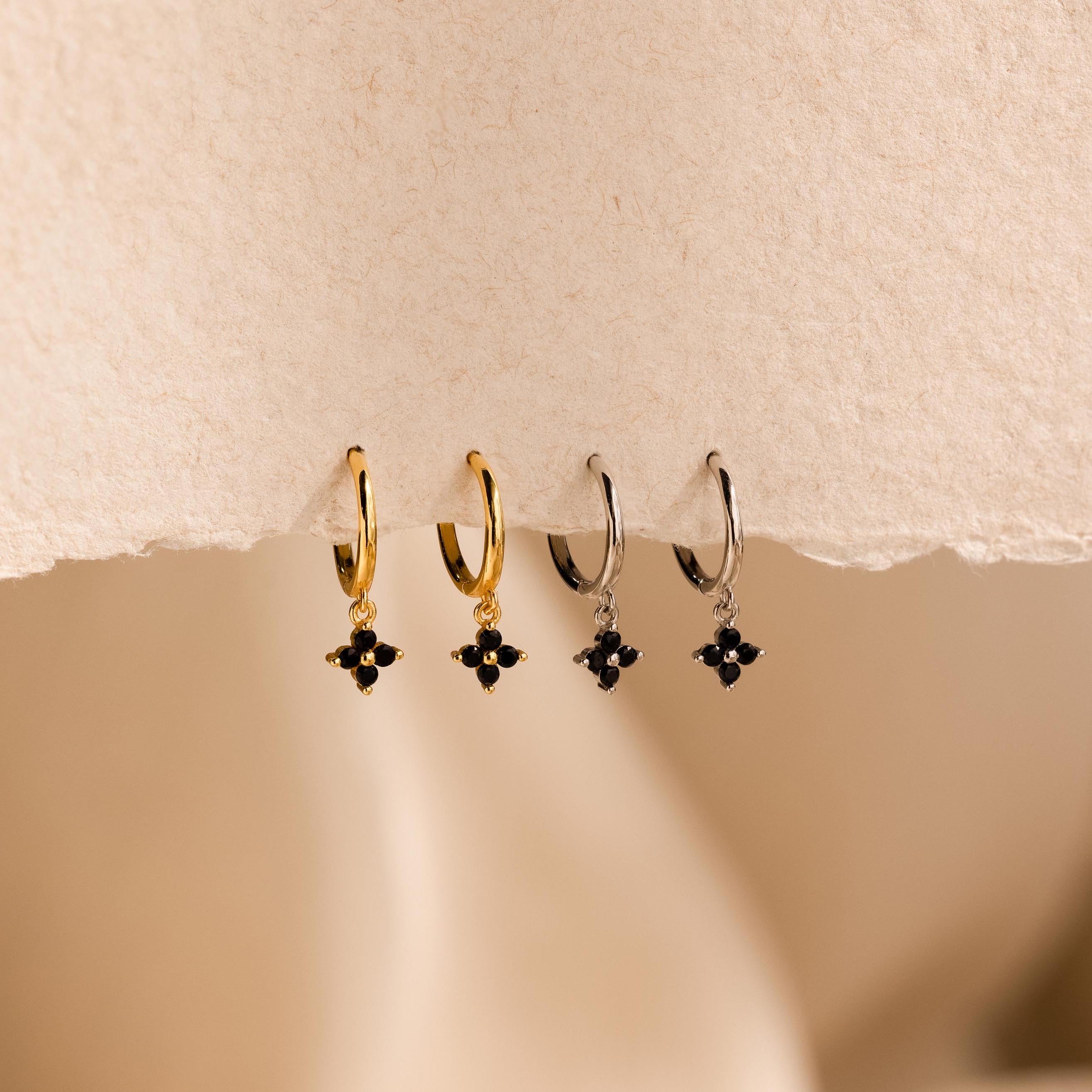 Two pairs of Black Ivy Flower Huggies—small hoop earrings in gold and silver, each adorned with a black gemstone cluster charm.