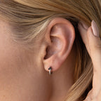 Close-up of a woman's ear wearing the Onyx Lily Huggies—dainty hoops featuring black onyx and clear stone accents.