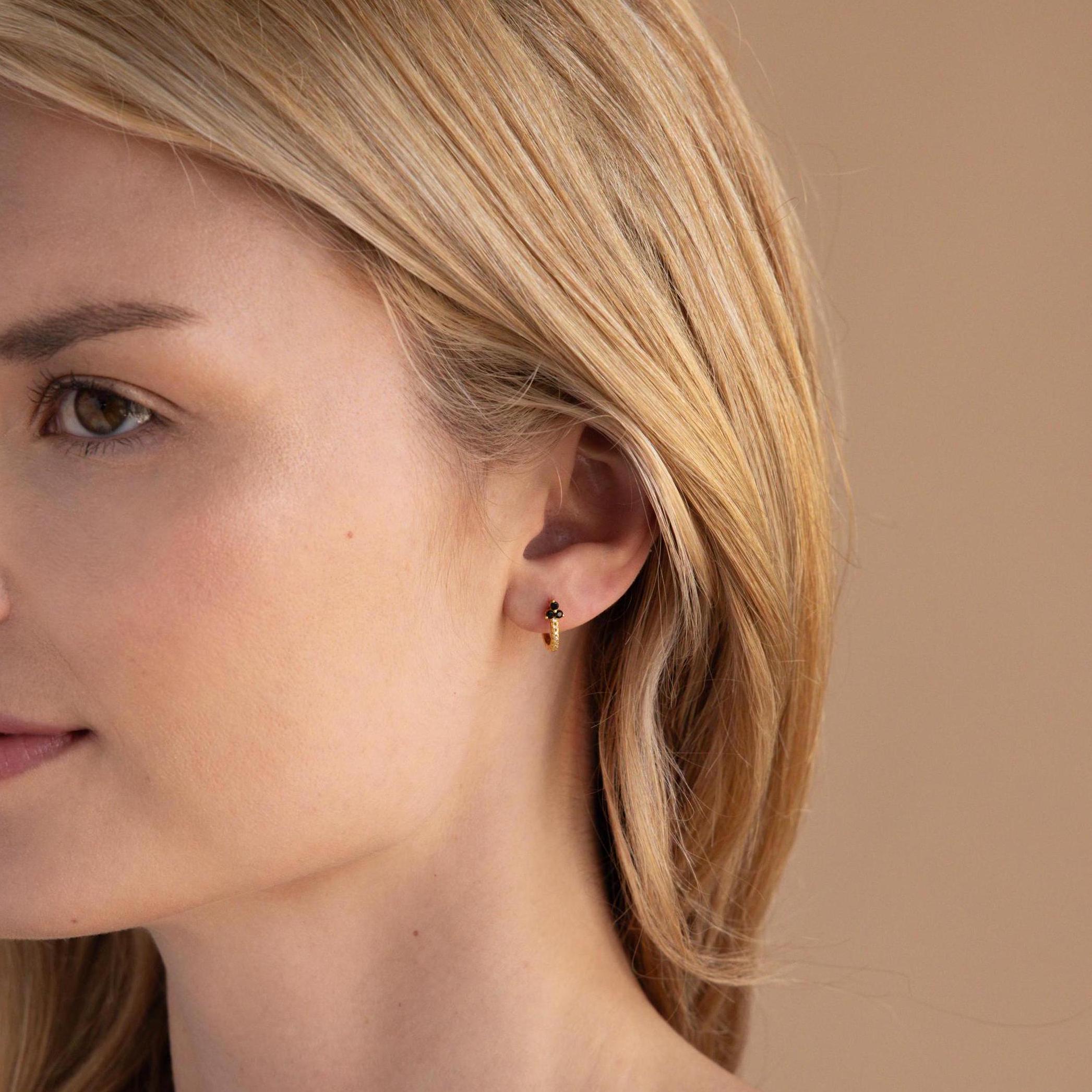 A close-up of a woman's face, delicately accented by the Onyx Lily Huggies—dainty hoops that bring an elegant touch of sophistication.