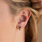 Close-up of a woman’s ear wearing Onyx Lily Huggies—delicate gold hoops accented with elegant black onyx beads.