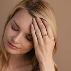 Woman with closed eyes touching her forehead, wearing the Black Baguette Diamond Ring in 18K Gold on her left hand—a true statement piece.