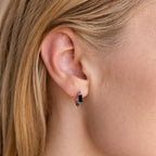 Close-up of a woman's ear wearing the Onyx Link Huggies, small silver chain hoop earrings with a rectangular black onyx gemstone.