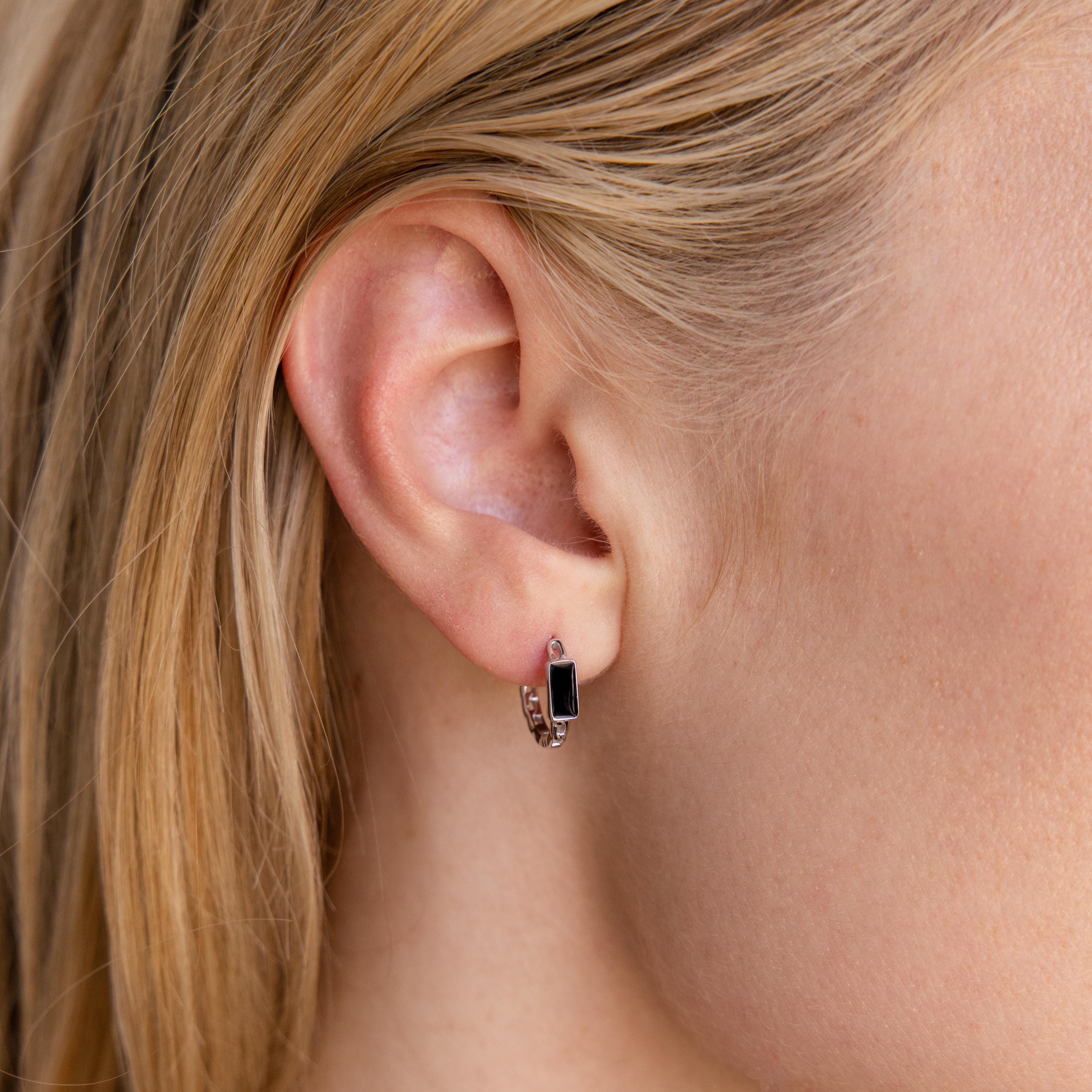 Close-up of a woman's ear wearing the Onyx Link Huggies, small silver chain hoop earrings with a rectangular black onyx gemstone.