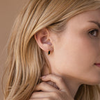 Close-up of a woman with blonde hair wearing the Onyx Link Huggies—small, rectangular gold earrings with black onyx gemstones—touching her neck.