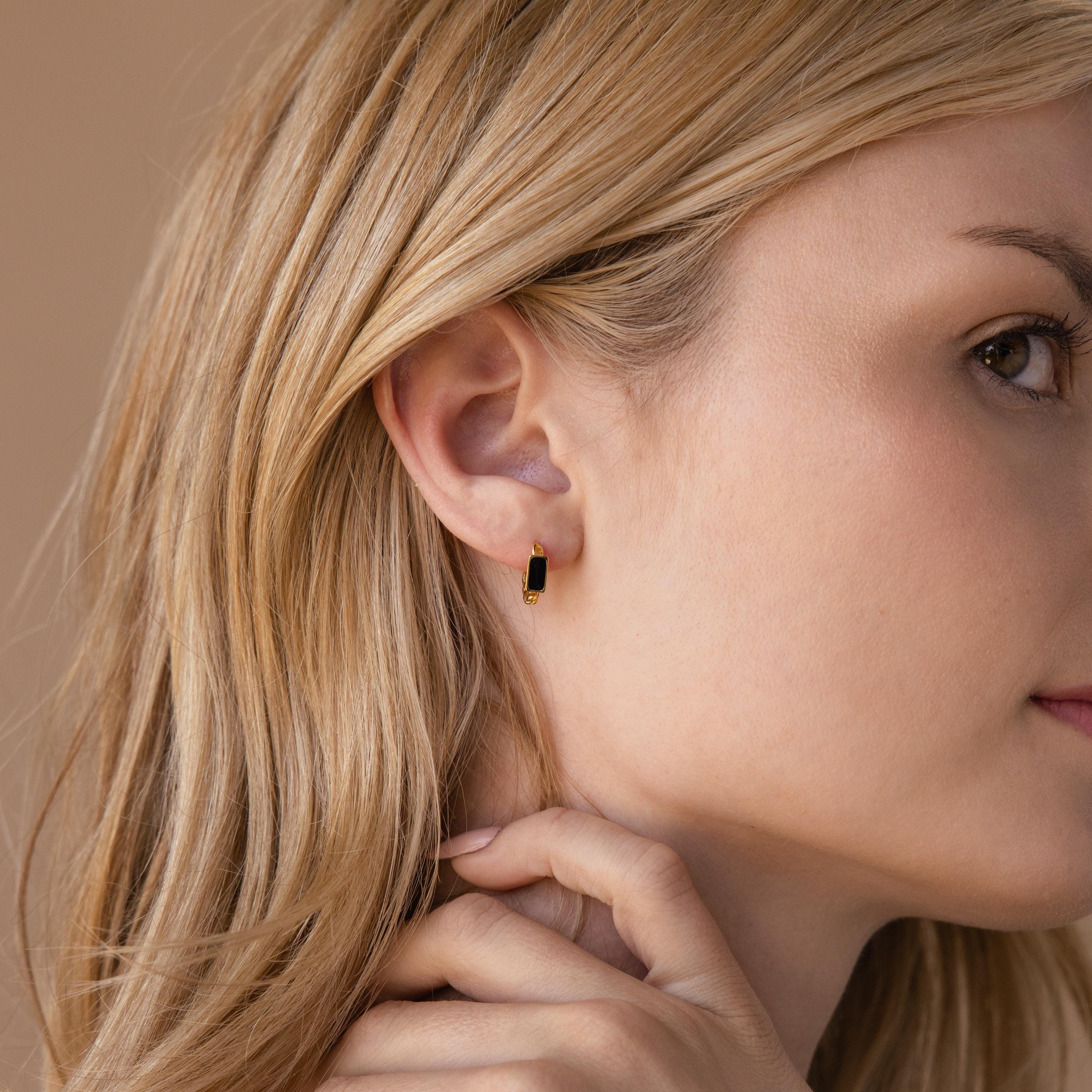 Close-up of a woman with blonde hair wearing the Onyx Link Huggies—small, rectangular gold earrings with black onyx gemstones—touching her neck.