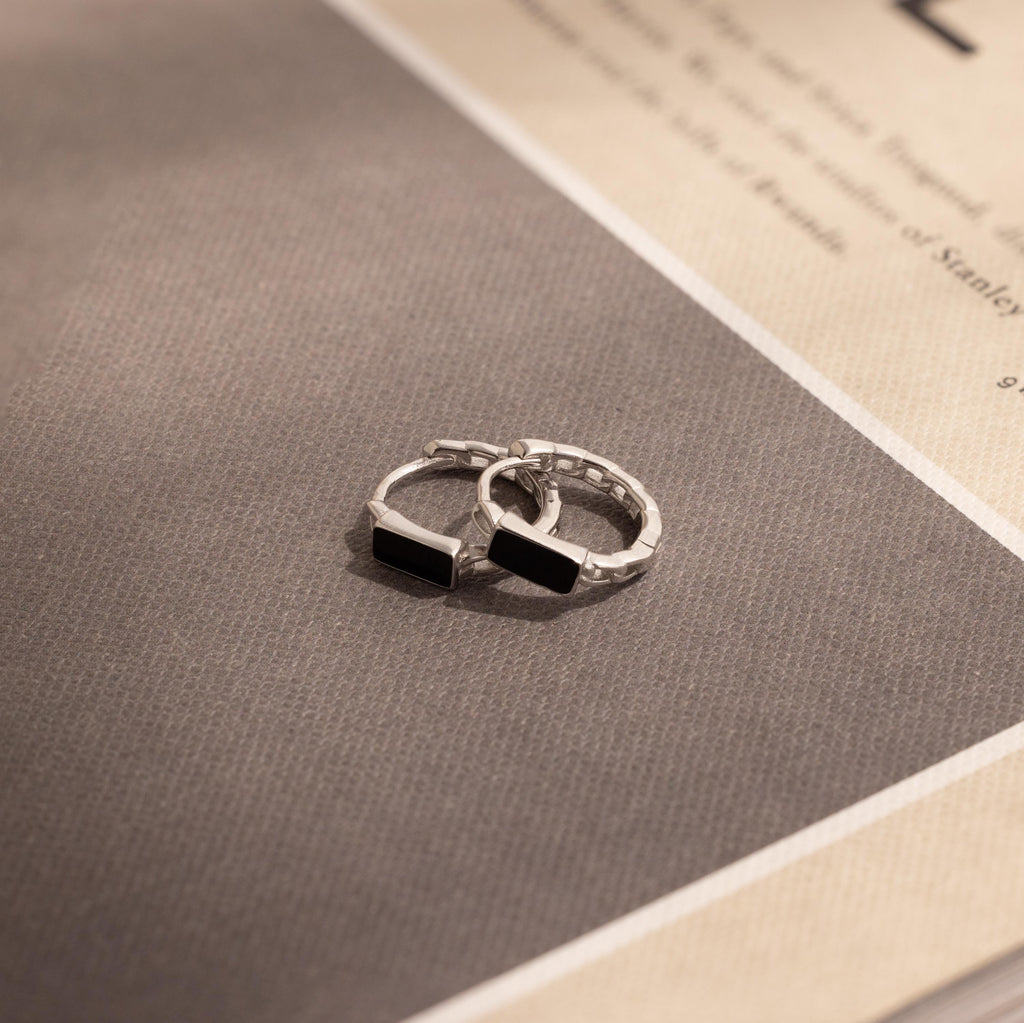A pair of rings on a book, their design reminiscent of the elegant Onyx Link Huggies.