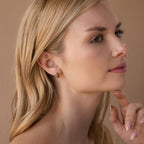 A woman with long blonde hair gazes thoughtfully to the side, wearing Chunky Onyx Pave Huggies.