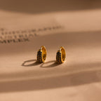 Chunky Onyx Pave Huggies—gold hoop earrings with black stones—cast bold shadows on a beige surface, blending modern style with classic elegance.