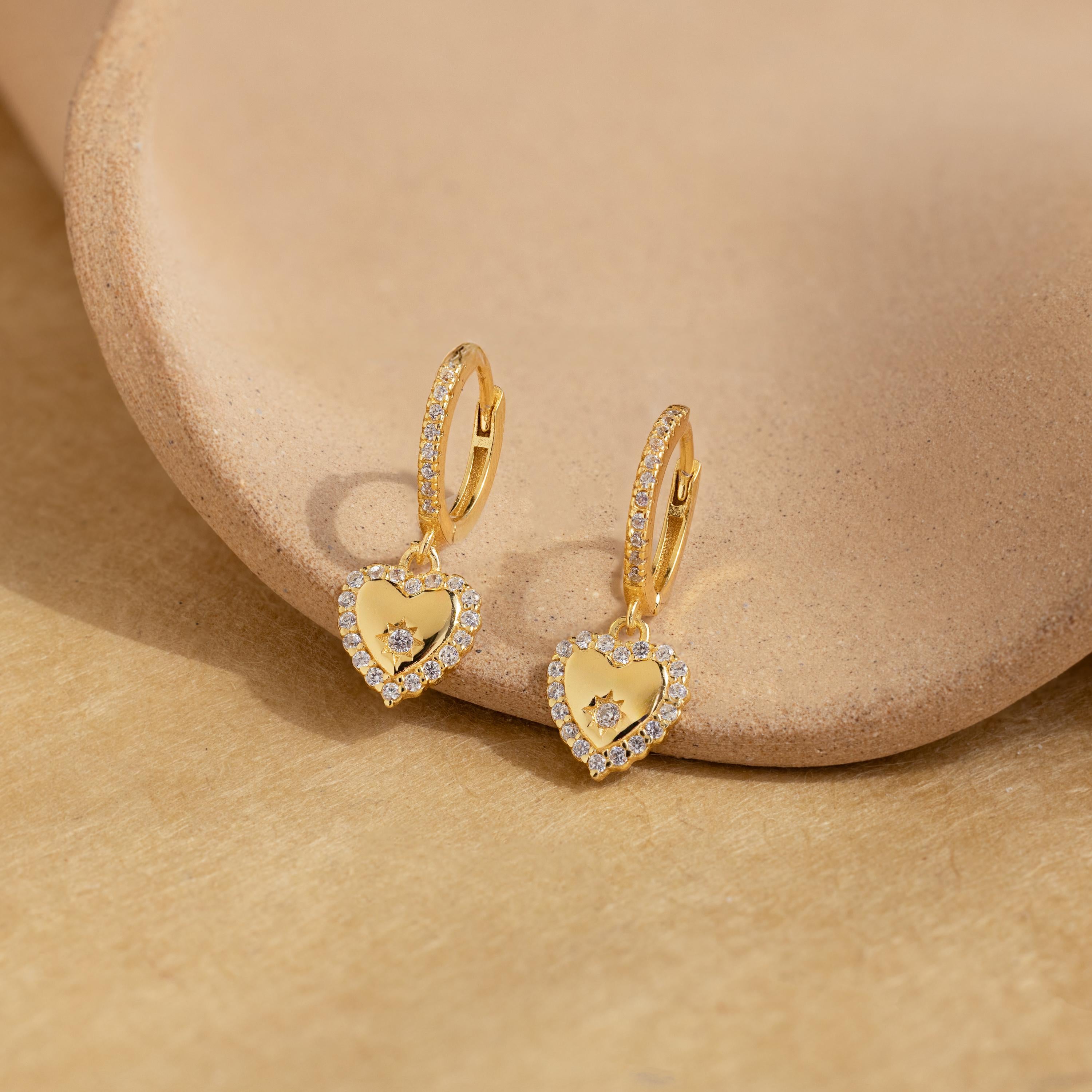 Pave Heart Drop Huggies with sparkling diamonds, shown on a neutral ceramic dish and tan surface—an elegant, romantic gift for anyone who loves timeless diamond earrings.