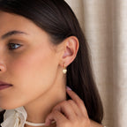 Woman with long dark hair wearing Pave Heart Drop Huggies, gently touching her ear—an elegant choice that makes a perfect romantic gift.