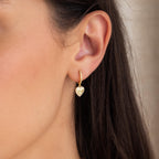 Close-up of a woman's ear wearing Pave Heart Drop Huggies—gold, heart-shaped earrings encrusted with sparkling diamonds. A romantic and elegant diamond earring gift choice.