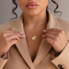 A woman in a beige blazer holds the Stylish Pearl Initial Heart Necklace with a gold butterfly charm delicately near her neck.