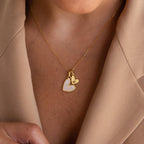 The Stylish Pearl Initial Heart Necklace, featuring a heart charm and personalized initial pendant, is styled on bare skin under a beige blazer.