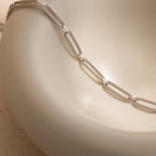 A Pave Link Chain Necklace in silver is draped over a smooth, cream-colored curved surface.