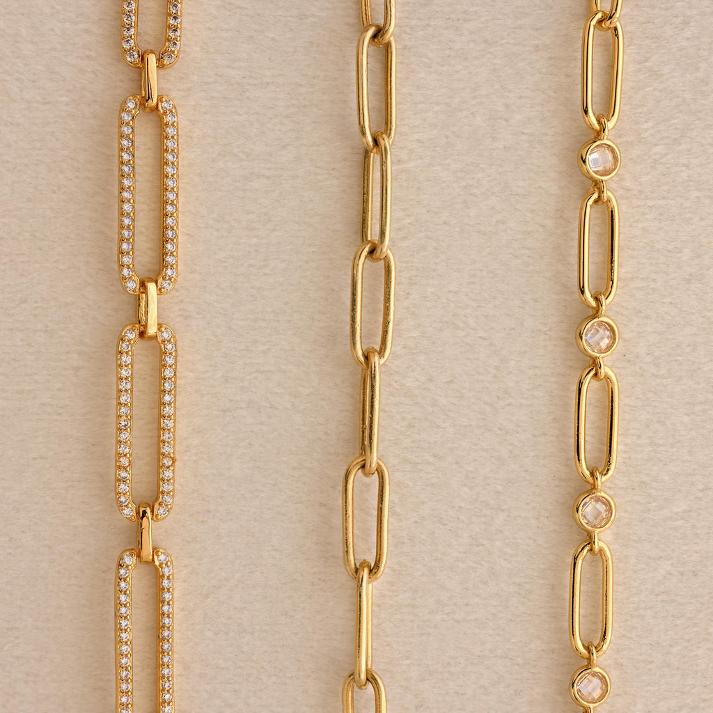 Three gold chain necklaces—a Pave Link Chain Necklace with sparkling diamonds, a plain chain, and one adorned with small round gems—are displayed on a neutral background.