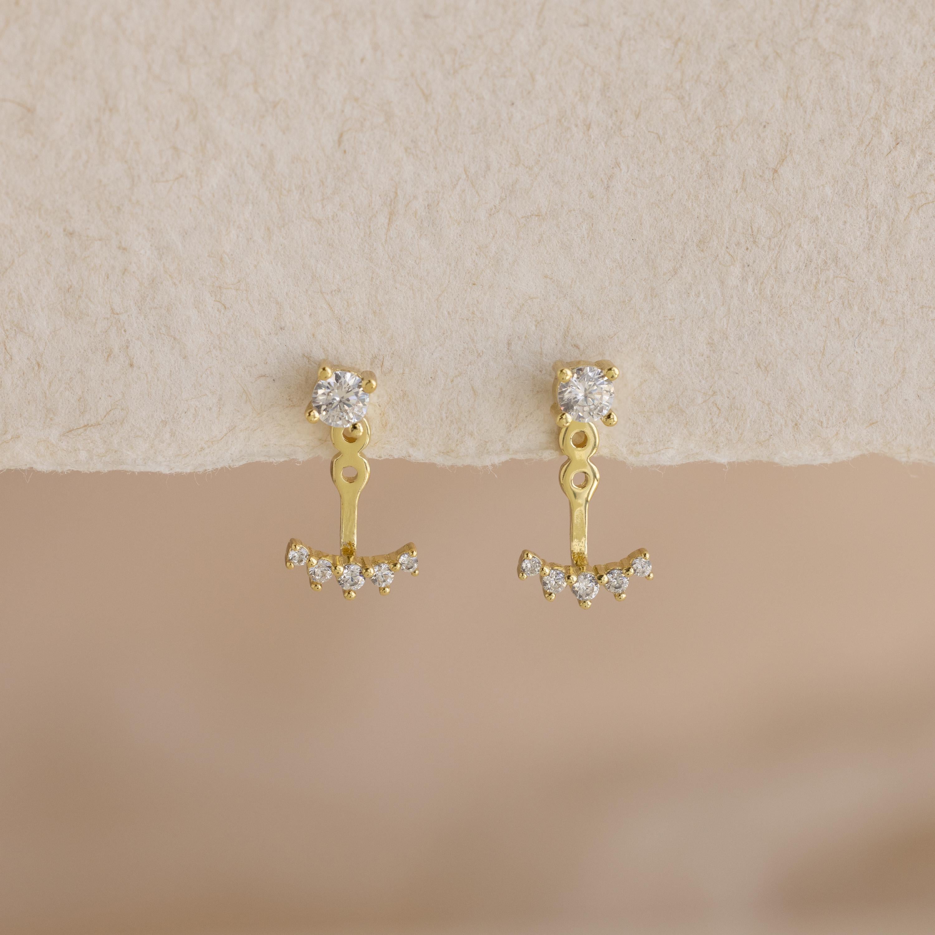 Round Diamond Ear Jackets in 18K Gold with brilliant-cut diamonds and delicate dangles are displayed on a textured cream surface.