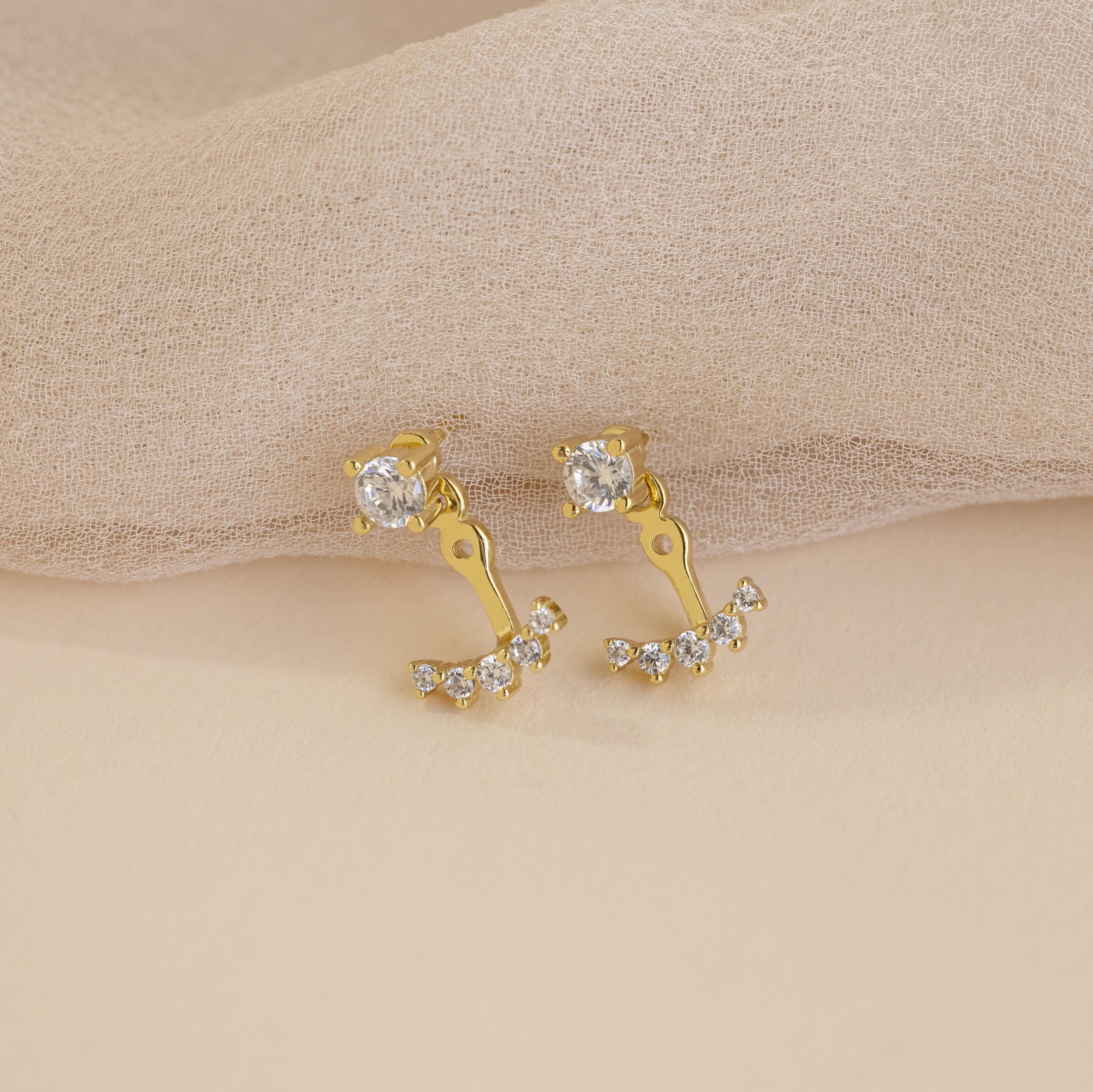 Round Diamond Ear Jackets in 18K Gold are displayed on a beige textured fabric background, highlighting the refined elegance and sparkle of these stylish earrings.