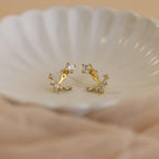 Diamond Cluster Ear Jackets featuring a front-back design and small sparkling stones are displayed on a white, scalloped dish—ideal for lovers of delicate earrings.