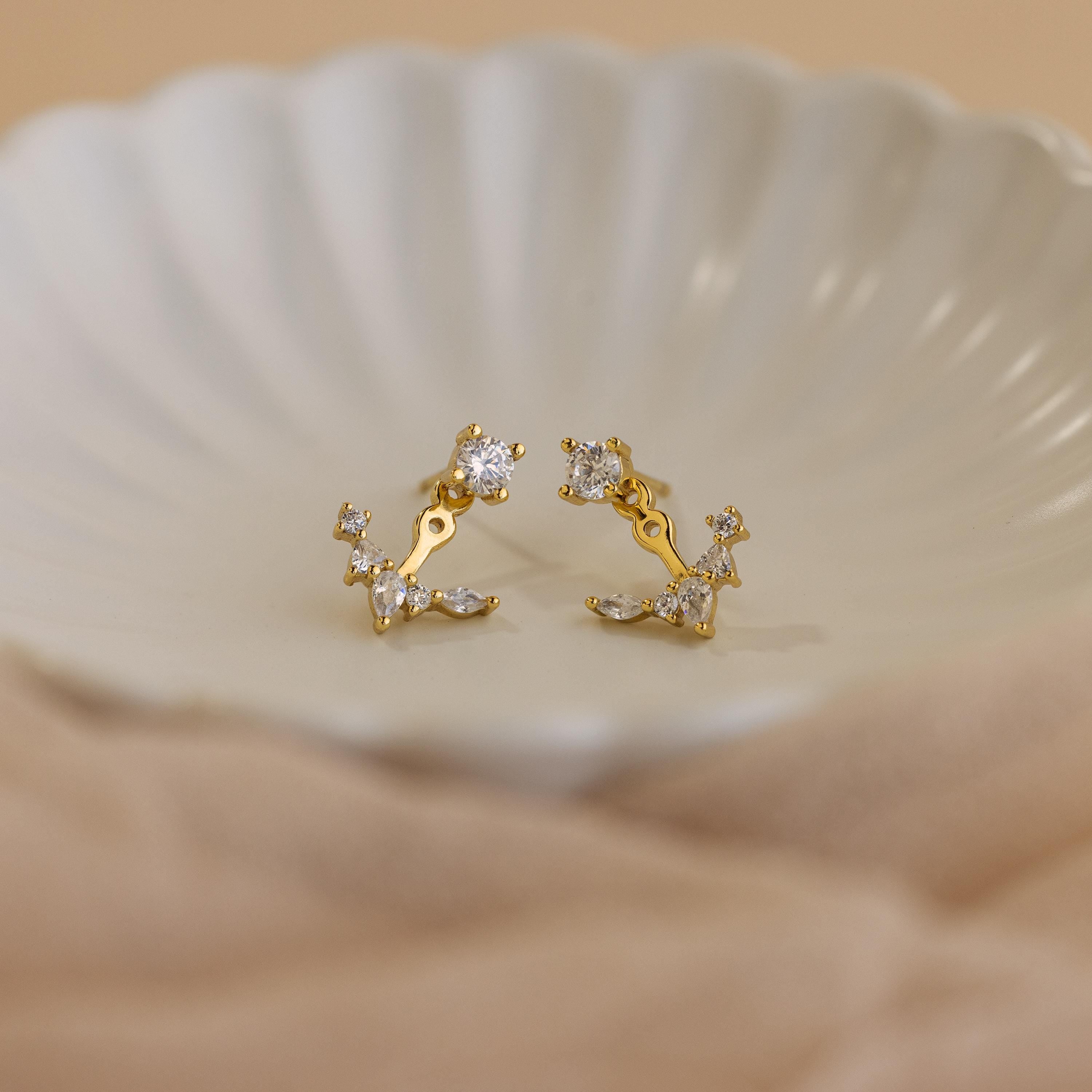 Diamond Cluster Ear Jackets featuring a front-back design and small sparkling stones are displayed on a white, scalloped dish—ideal for lovers of delicate earrings.