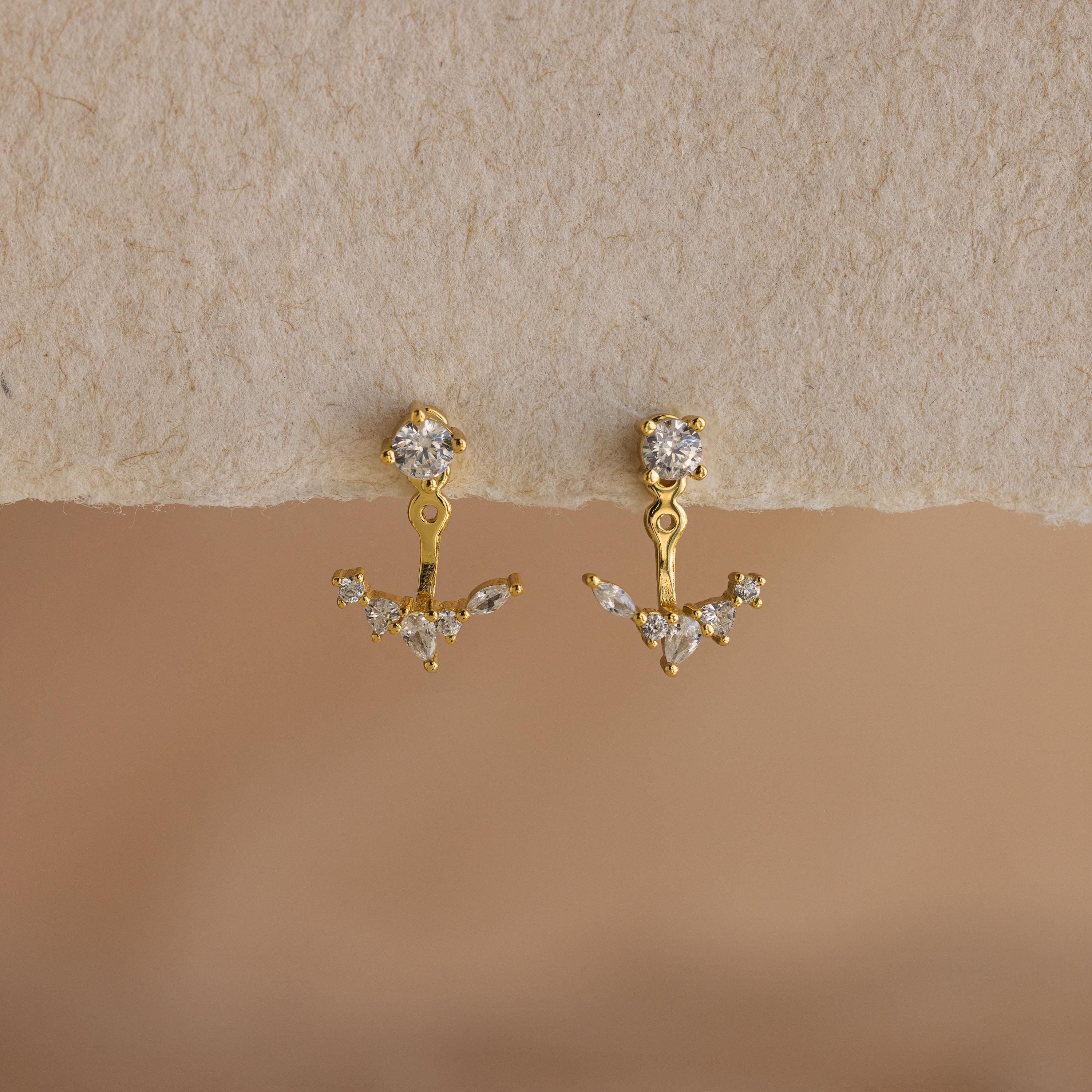 Diamond Cluster Ear Jackets: Gold earrings with clear gemstones in a floral-inspired front-back design, shown on a textured beige surface.