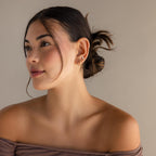 A woman wearing Marquise Pave Huggies looks away from the camera, the bezeled marquise gemstones on her earrings catching the light.