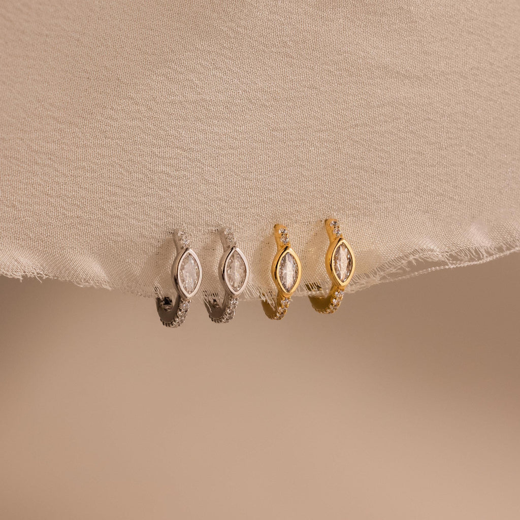 Two pairs of Marquise Pave Huggies, featuring elegant small hoops in silver and gold, displayed on light beige fabric.