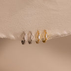 Two pairs of Marquise Pave Huggies, featuring elegant small hoops in silver and gold, displayed on light beige fabric.