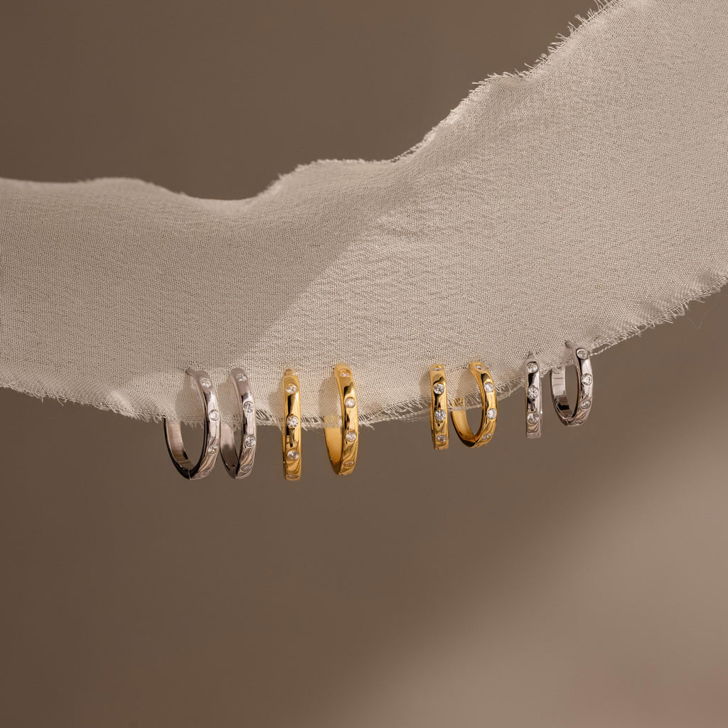 A collection of gold and silver rings, featuring elegant diamond hoop earrings and chic Mini Diamond Sprinkle Huggies.