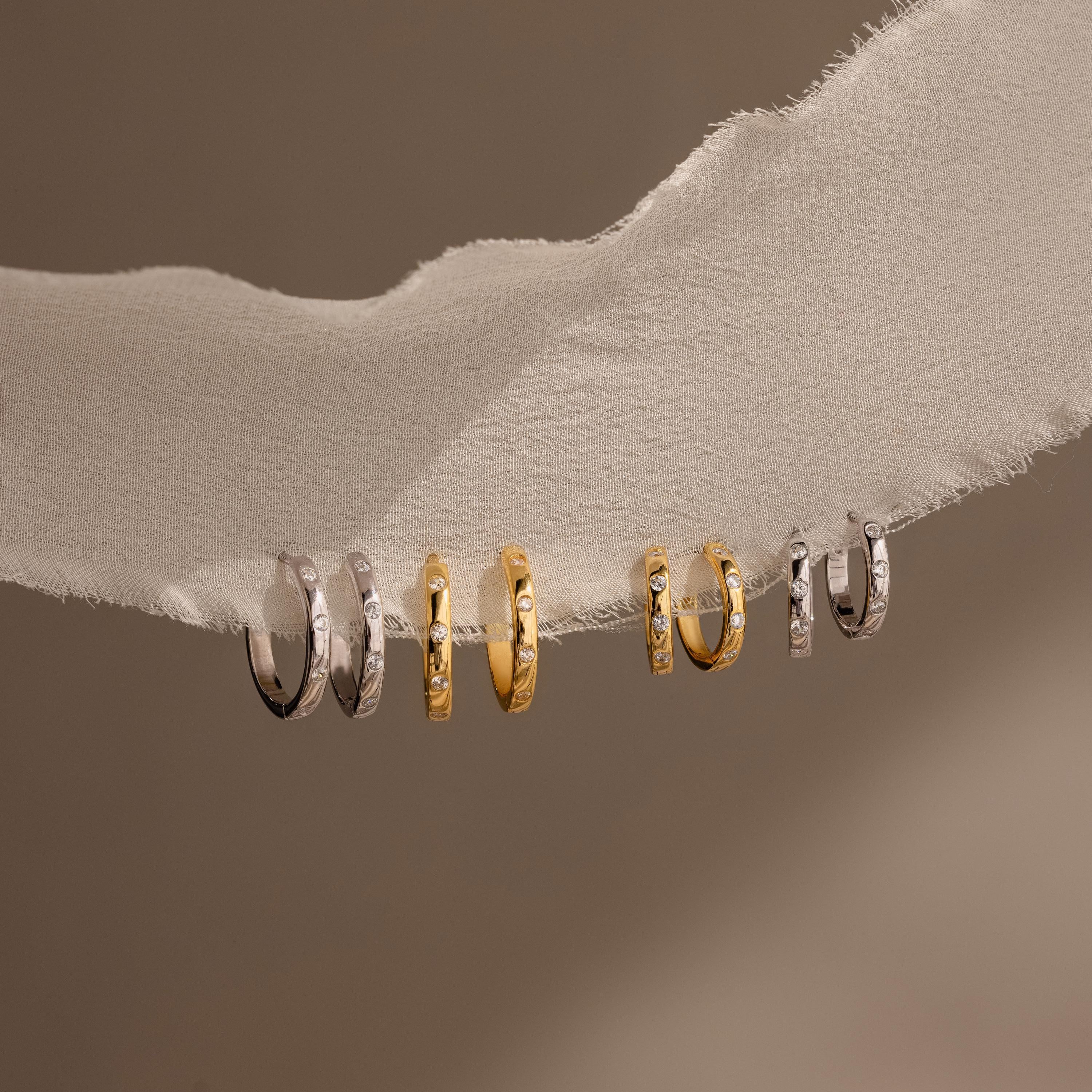 A collection of gold and silver rings, featuring elegant diamond hoop earrings and chic Mini Diamond Sprinkle Huggies.