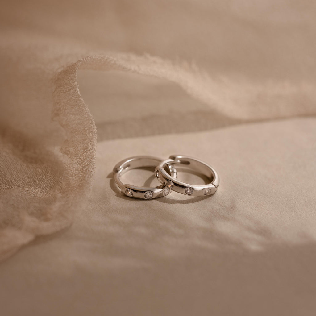 Two silver rings with small diamonds rest on soft beige fabric, their sparkle reminiscent of our Mini Diamond Sprinkle Huggies and delicate diamond hoop earrings.