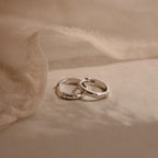 Two silver rings with small diamonds rest on soft beige fabric, their sparkle reminiscent of our Mini Diamond Sprinkle Huggies and delicate diamond hoop earrings.