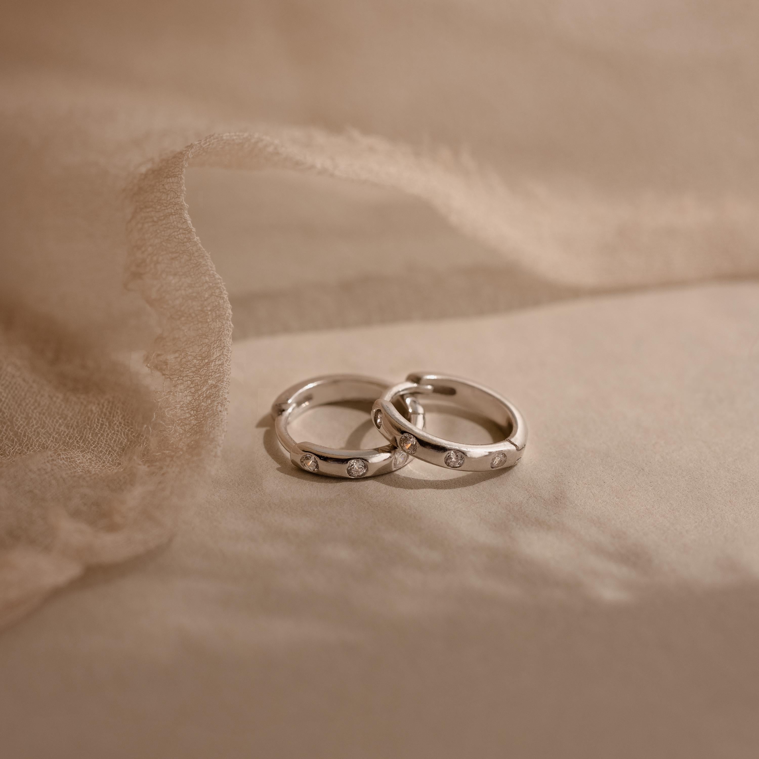 Two silver rings with small diamonds rest on soft beige fabric, their sparkle reminiscent of our Mini Diamond Sprinkle Huggies and delicate diamond hoop earrings.