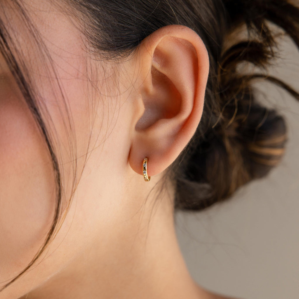 A woman's ear adorned with Mini Diamond Sprinkle Huggies; her hair is tied back, and a loose strand gently frames her face.